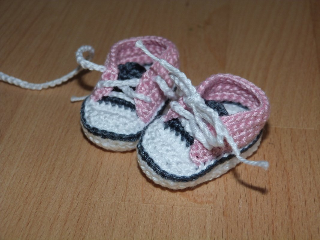 Nahaufnahme von zwei gehäkelten Mini-Sneakern mit Schnürsenkeln und kontrastfarbener Sohle