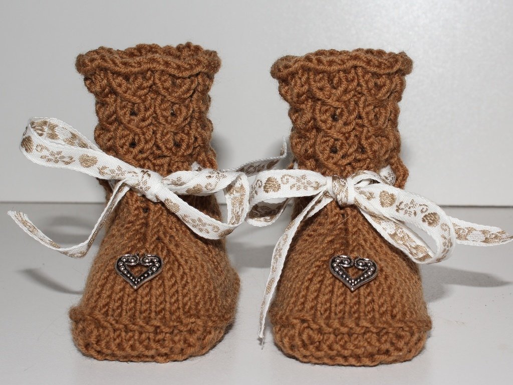 Braune gestrickte Babyschuhe mit gewelltem Schaft, weißen Schleifenbändern und kleinen Herzknöpfen