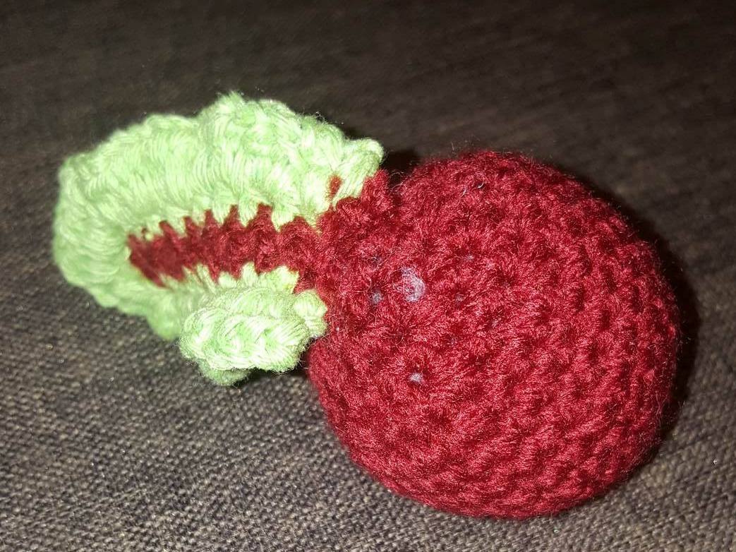Gehäkelte rote Kirsche mit grünen Blättern auf dunklem Stoff