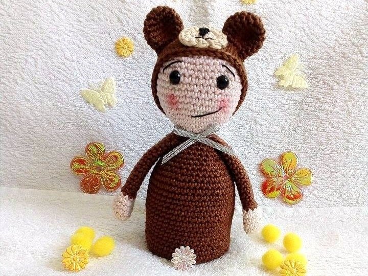 Gehäkelte Amigurumi-Puppe in braunem Bärenkostüm mit Schleife und rosigen Wangen