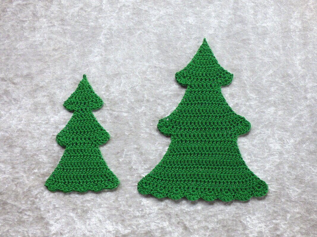 Zwei gehäkelte grüne Tannenbaum-Applikationen in kleiner und großer Ausführung auf hellem Hintergrund