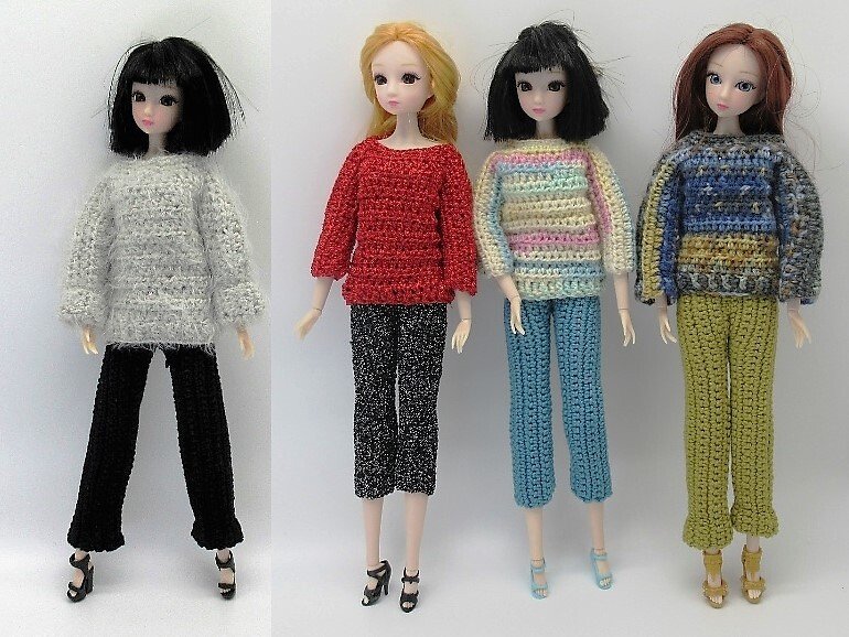 Vier Puppen tragen gehäkelte Pullover und Hosen in unterschiedlichen Farben und Mustern