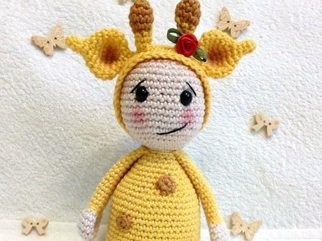 Gehäkelte Amigurumi-Puppe in gelbem Giraffen-Kostüm mit Hörnern und rosigen Wangen