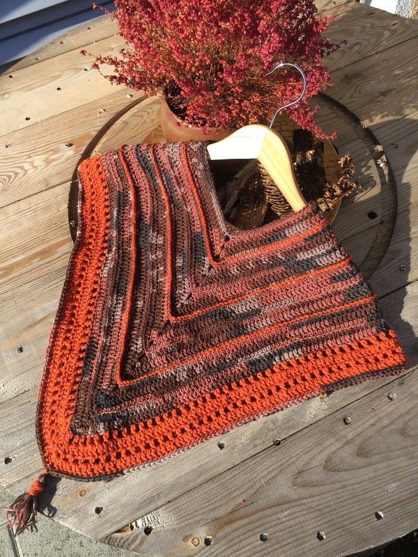 Gehäkelter Damen-Poncho in Rostorange, Braun und Anthrazit mit Quaste auf Holztisch