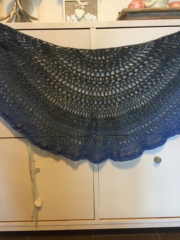 Halbrundes gehäkeltes Tuch in Anthrazit- bis Blautönen mit Lochmuster und Muschelsaum, auf einem weißen Schrank drapiert.