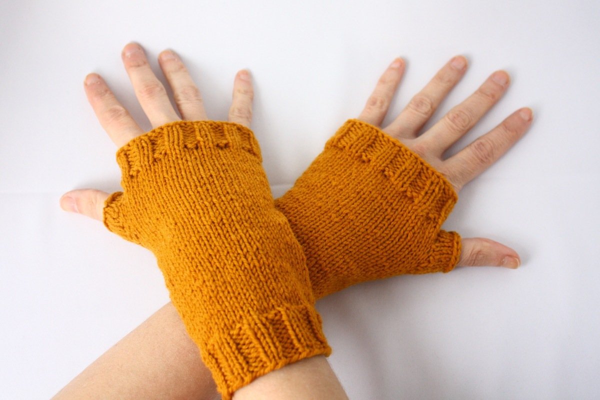 Eine Person trägt senfgelbe, gestrickte fingerlose Handschuhe an beiden Händen.