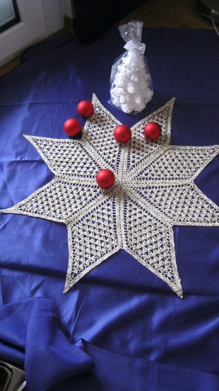 Filigranes gehäkeltes Stern-Deckchen in Creme auf violettem Untergrund mit roten Kugeln