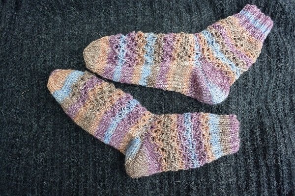 Gestricktes Sockenpaar mit Rippenbündchen, Streifen und Lochmuster auf dunklem Stoff