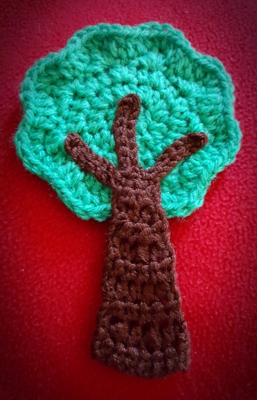 gehäkelte Baum-Applikation mit grünem Blattwerk und braunem Stamm auf rotem Stoff