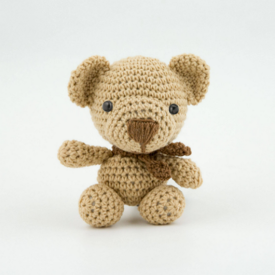 Beiger gehäkelter Amigurumi-Teddybär mit brauner Nase und Schal vor weißem Hintergrund