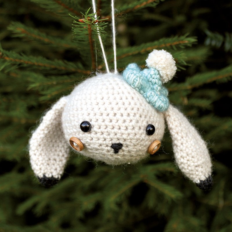 Weißer gehäkelter Hasen-Anhänger mit hellblauer Mütze an einem Tannenzweig