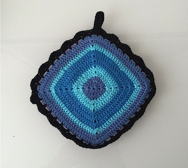 Quadratischer gehäkelter Topflappen mit blau-türkisen Farbringen, schwarzem Rand und Aufhängeschlaufe