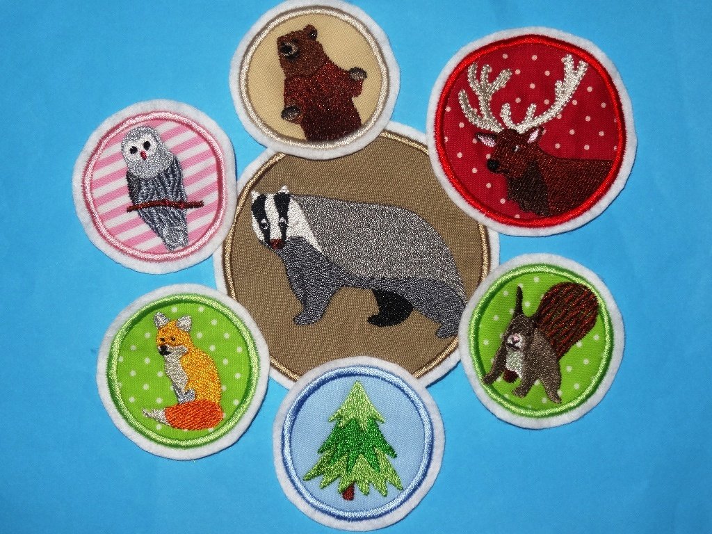 Runde gestickte Applikationen mit Dachs, Hirsch, Bär, Fuchs, Eule, Eichhörnchen und Tannenbaum auf farbigem Stoff.