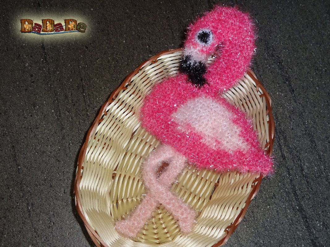 Rosa flauschiger gehäkelter Flamingo in kleinem Korb auf dunklem Untergrund