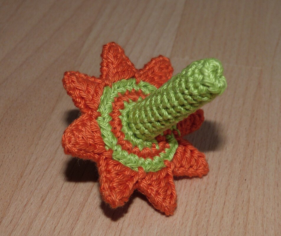 Gehäkelter Kreisel in Orange und Grün mit sternförmiger Basis auf Holzoberfläche.