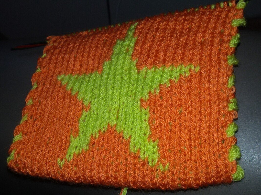 Gestricktes Quadrat mit leuchtend grünem Stern auf orangefarbenem Grund