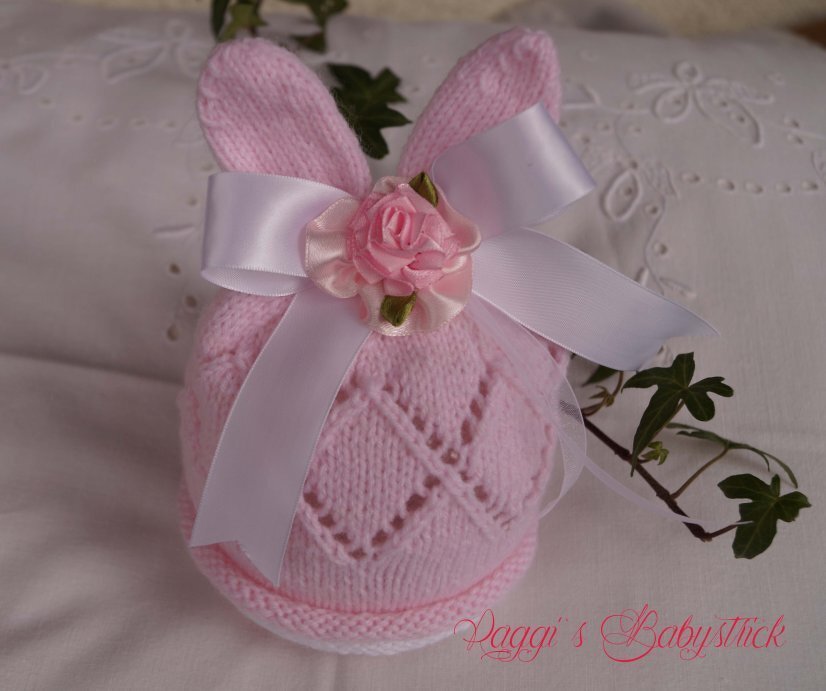 rosa gestrickte Babymütze mit Hasenohren, Diamant‑Ajourmuster und weißer Satin‑Schleife mit rosa Rose