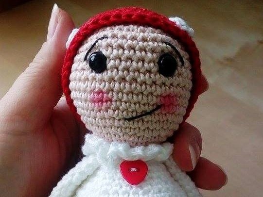 Gehäkelte Puppe in Rot und Weiß mit herzförmigem Knopf und lächelndem Gesicht, Nahaufnahme