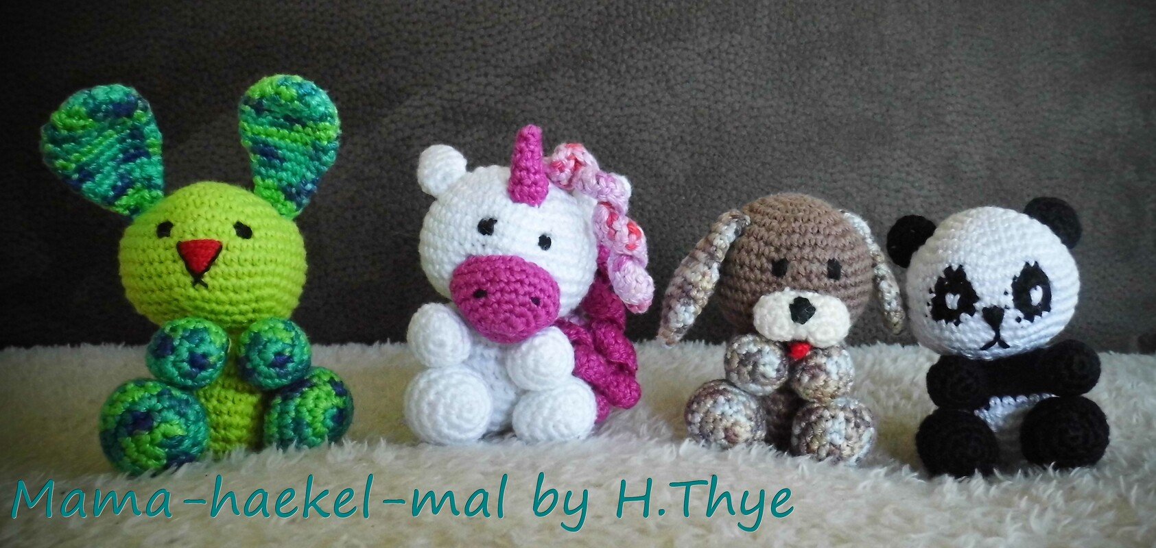 Vier gehäkelte Amigurumi-Tiere: grüner Hase, weißes Einhorn, brauner Hund und schwarz-weißer Panda auf flauschigem Untergrund.