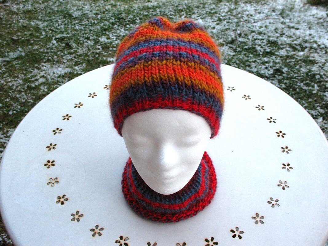 Bunte gestrickte Mütze und Loop auf weißem Schaufensterkopf vor leicht verschneitem Rasen