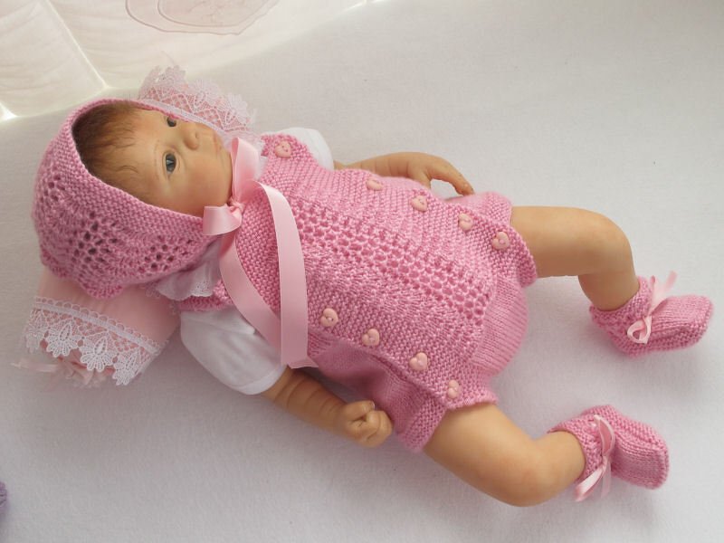 Liegende Babypuppe im rosa Strickset mit Strampler, Häubchen und Schühchen mit Bändchen