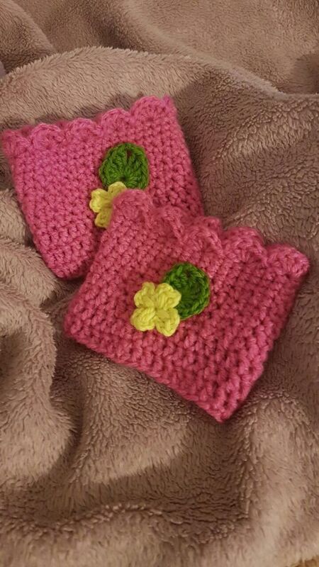 Zwei pinke gehäkelte Damen-Beinstulpen mit grüner und gelber Blumen-Applikation auf beigem Stoff