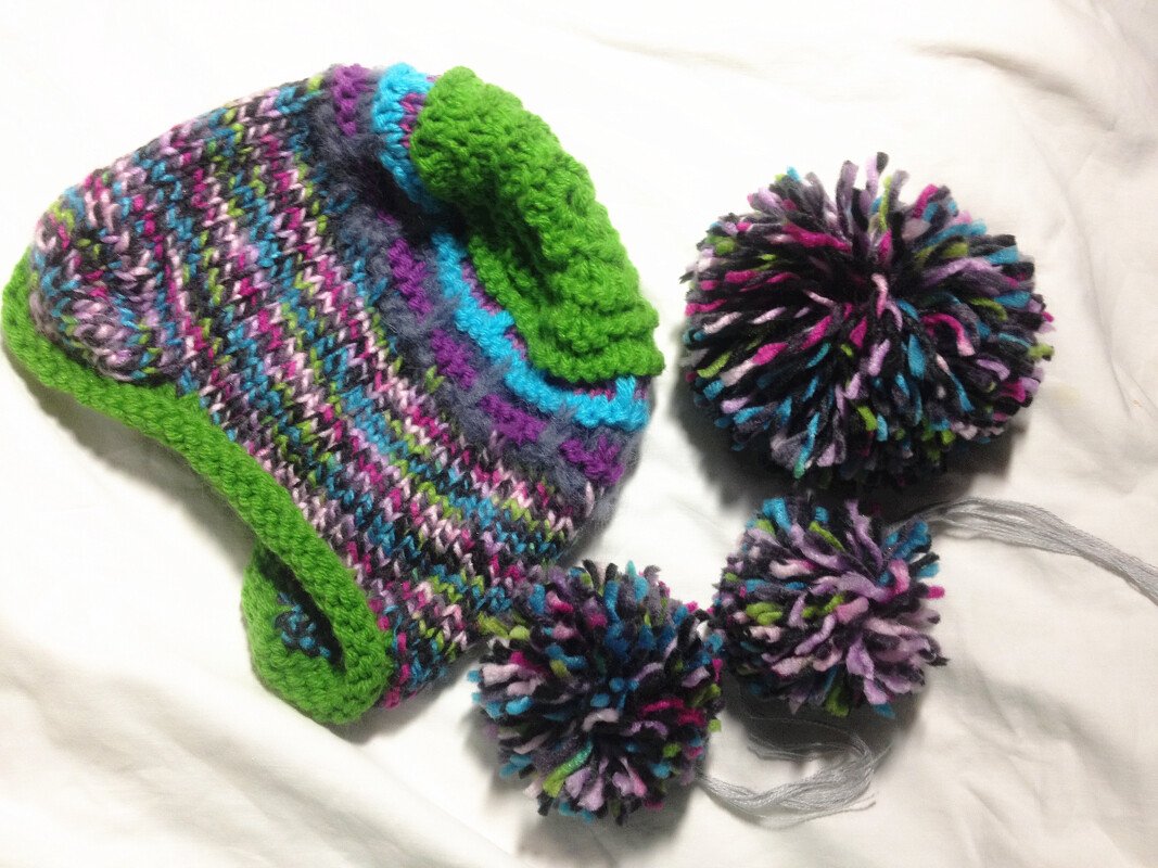 Mehrfarbige gestrickte Kindermütze mit leuchtend grüner Krempe und drei passenden Bommeln