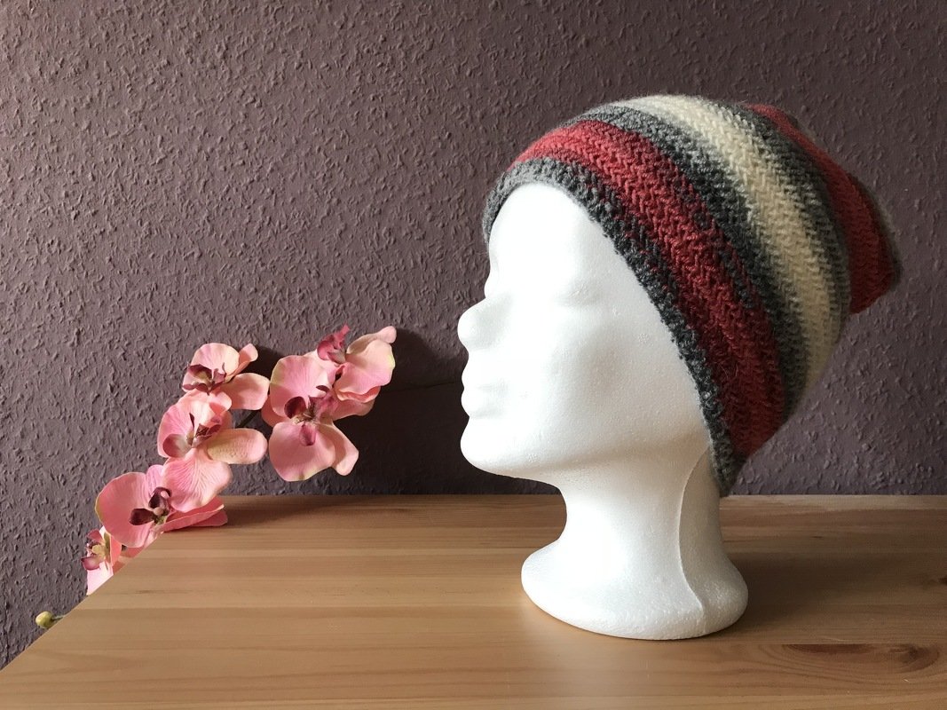 Unisex Slouch‑Mütze gestrickt mit breiten rostroten, cremefarbenen und grauen Streifen auf weißem Displaykopf vor violetter Wand