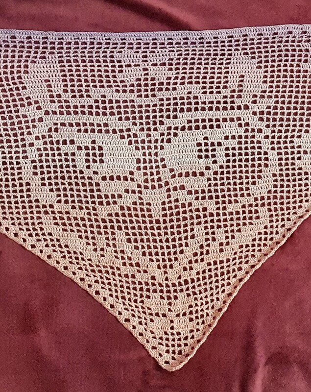 helles gehäkeltes Dreieckstuch im Filetmuster mit symmetrischem Tiermotiv auf dunklem Untergrund