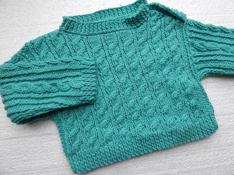 Türkisfarbener gestrickter Kinderpullover mit Zopfmuster und Stehkragen, flach liegend.