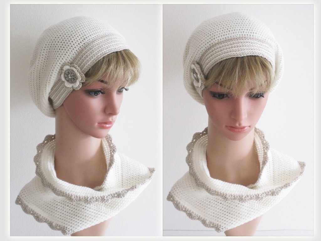 Gehäkeltes cremeweißes Barett mit Blumen-Applikation und passender Halswärmer mit beigem Wellenrand auf einer Schaufensterpuppe.