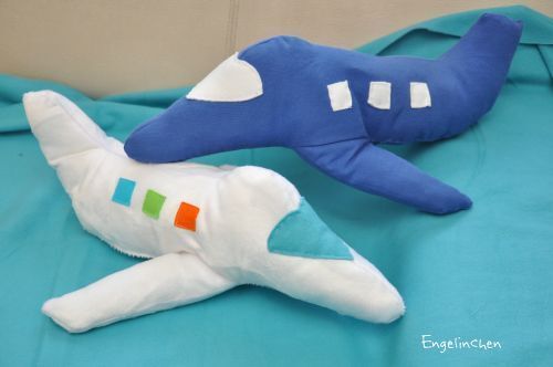 Zwei selbstgenähte Stoffflugzeuge, eines blau und eines weiß, auf türkisem Stoff