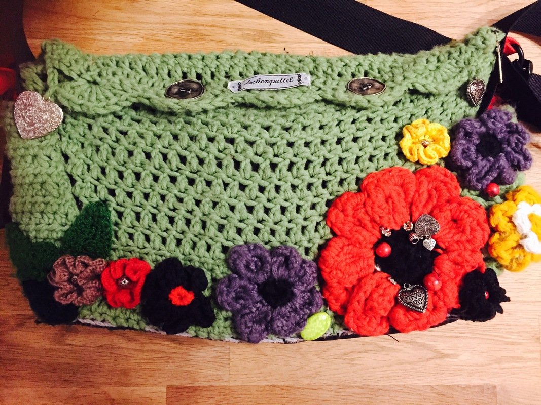 Hellgrüne gehäkelte Umhängetasche mit bunten Häkelblumen und kleinen Herzanhängern