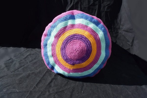 Runde gehäkelte Umhängetasche mit konzentrischen Streifen in Pink, Violett, Gelb, Türkis und Hellblau auf dunklem Hintergrund