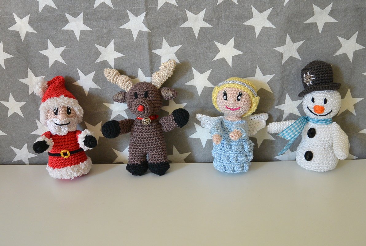Vier gehäkelte Weihnachtsfiguren (Weihnachtsmann, Rentier, Engel, Schneemann) vor grauem Stoff mit weißen Sternen