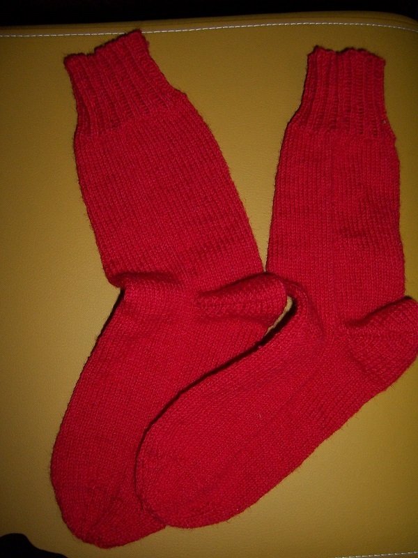 Zwei rot gestrickte Socken, glatt rechts mit Rippenbündchen auf hellem Untergrund