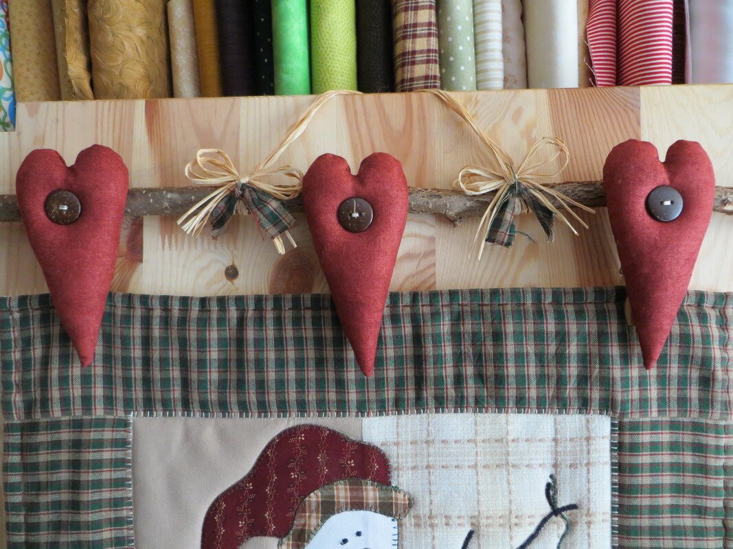 Drei längliche, rotbraune Stoffherzen mit Knöpfen an einem Ast