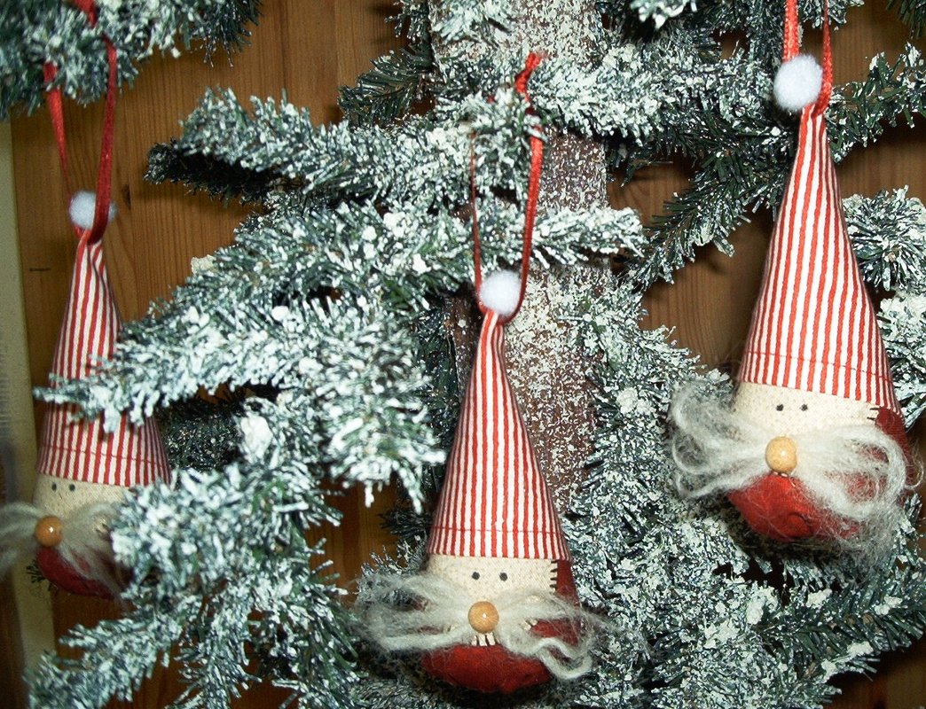 Detaillierte Ansicht von drei genähten Wichtel-Anhängern mit gestreiften Mützen und kleinen Nasen an einem verschneiten Weihnachtsbaum.