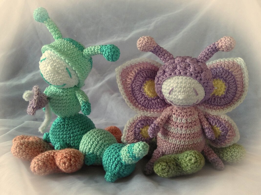 Handgehäkelte mintgrüne Raupe und lila-rosa Schmetterling (Amigurumi) auf hellem Tuch