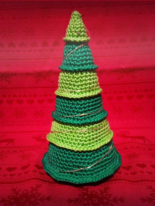 Kompakter konischer Häkelbaum aus hell- und dunkelgrünen Häkelringen mit goldfarbener Schnur vor rotem Stoff