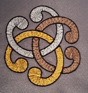 Stickerei eines verschlungenen keltischen Knotens in Gold, Silber und Bronze auf grauem Stoff