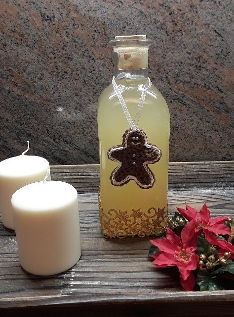 Glasflasche mit Korken und gehäkeltem Lebkuchenmann als Anhänger, auf Holztablett mit weißen Kerzen und rotem Weihnachtsstern