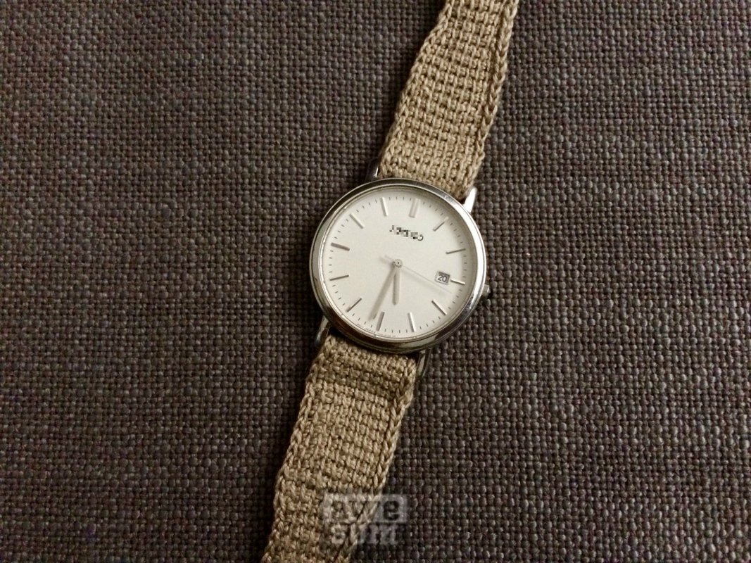 Armbanduhr mit beigem gehäkeltem Uhrenband auf dunkelgrauem Stoff