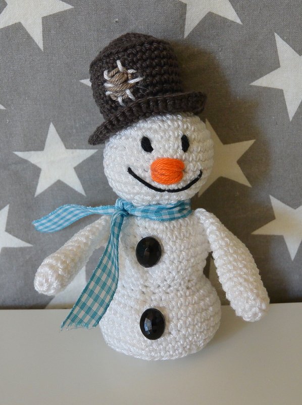 Gehäkelter Schneemann mit braunem Hut und blau-weiß kariertem Schal vor Sternenmuster