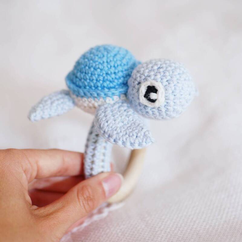 Hand holding pale blue crocheted turtle rattle attached to a wooden ring