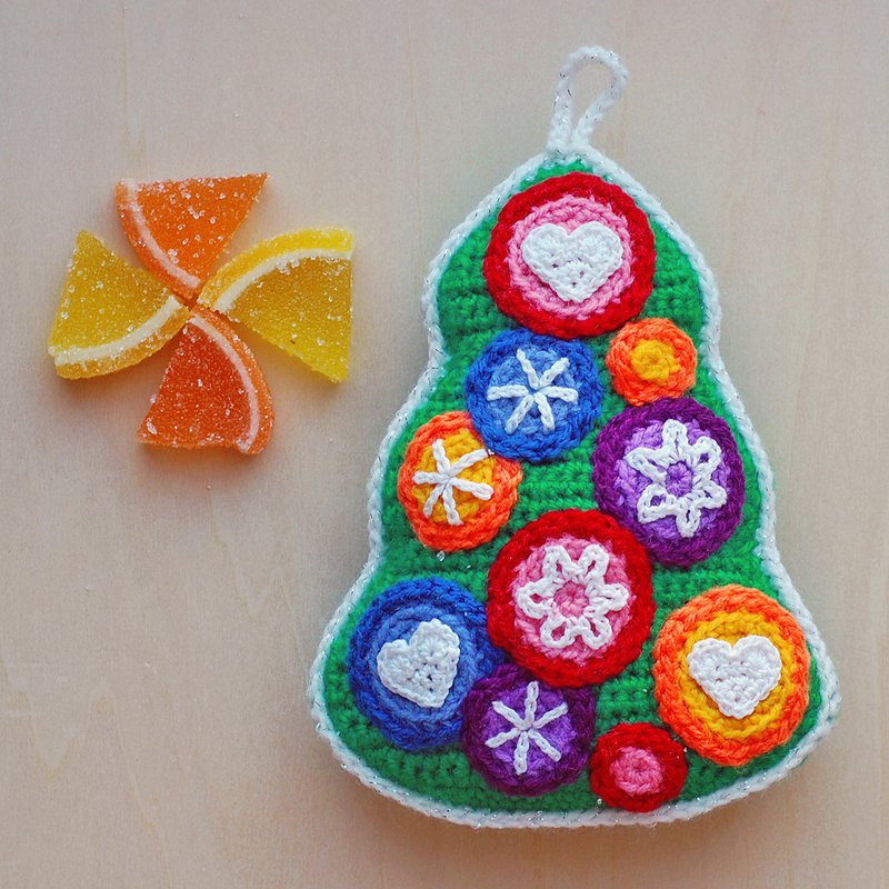 Green crocheted Christmas tree ornament with colorful round motifs and white border, next to orange and yellow jelly candies.