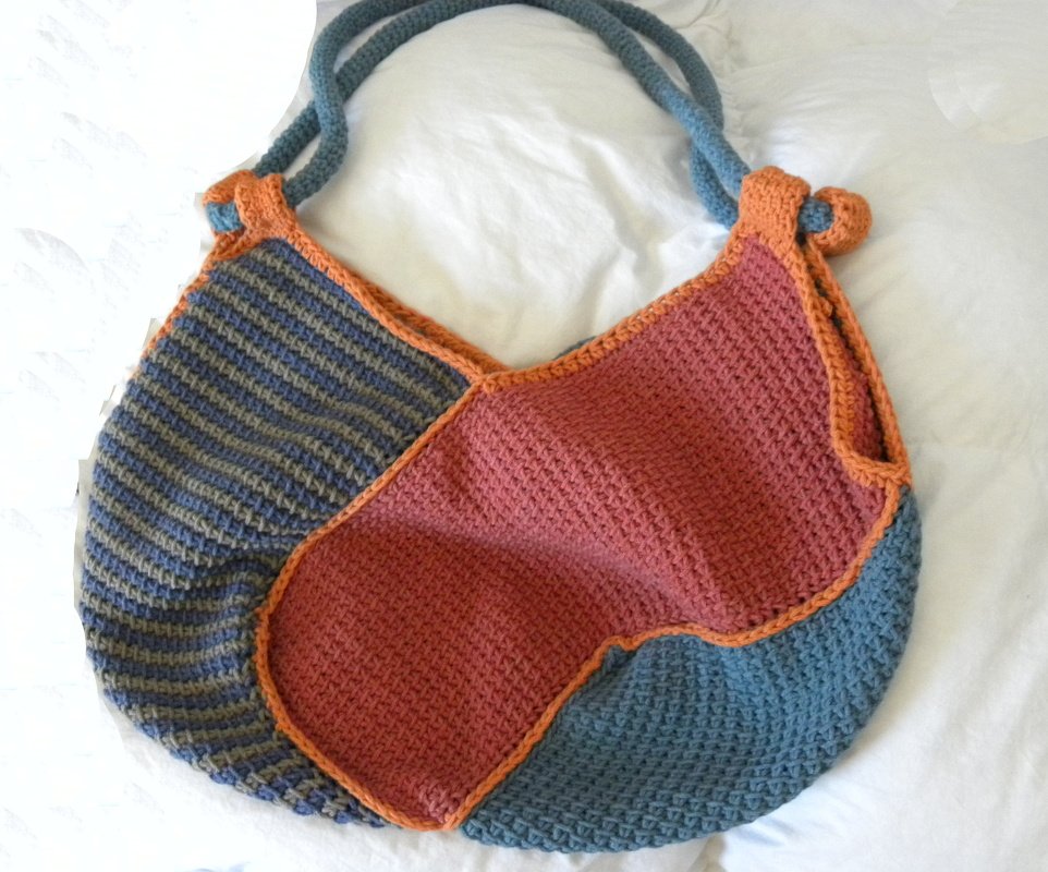 Gehäkelte Umhängetasche mit Terrakotta-, Hellblau- und gestreiften Graublau-Flächen, orangefarbener Einfassung und blauen Tragegriffen.