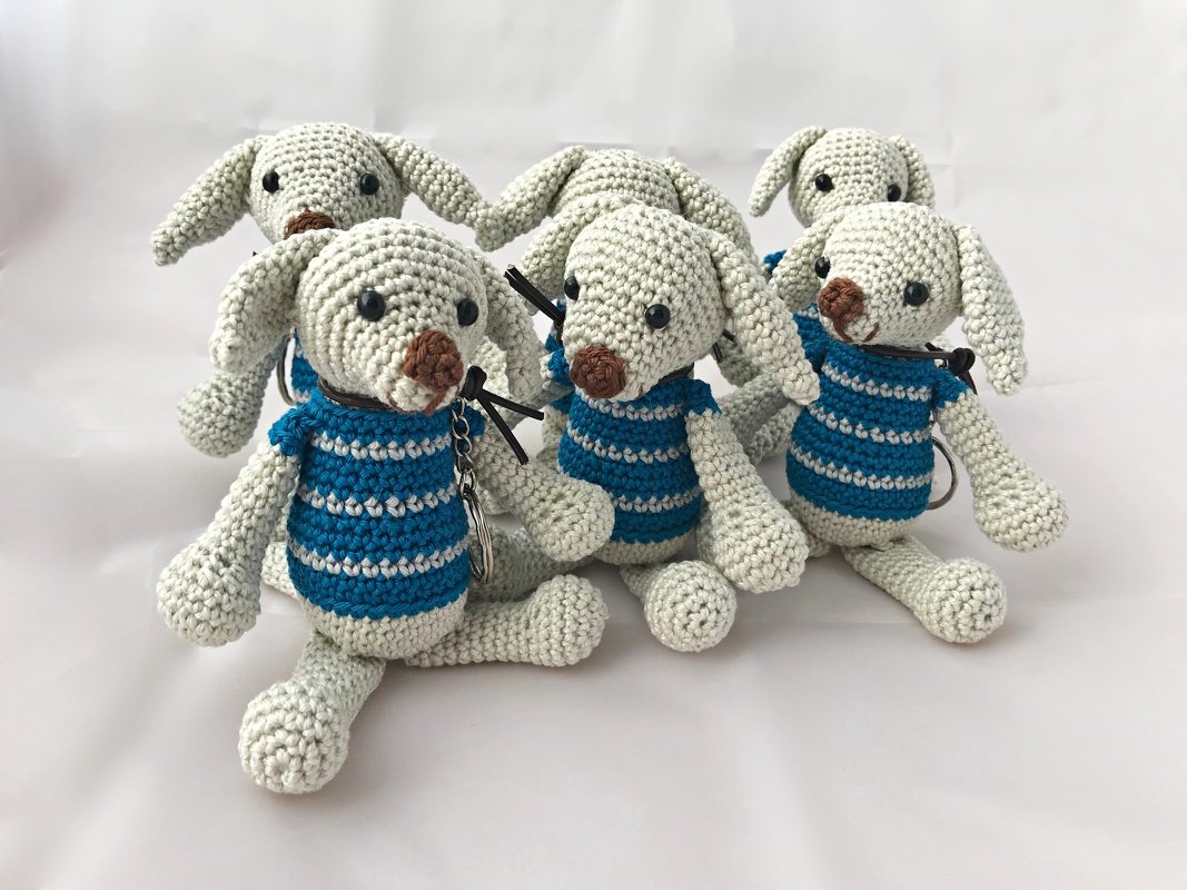 Sechs gehäkelte Hunde-Schlüsselanhänger mit blau-weiß gestreiften Oberteilen auf weißem Hintergrund.