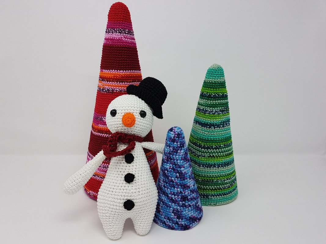 Gehäkelter Amigurumi-Schneemann mit schwarzem Hut und drei bunten gehäkelten Kegelbäumen