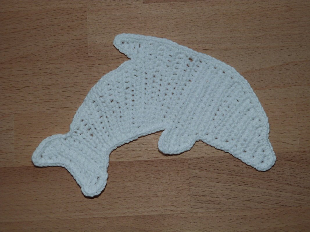 Weiße handgehäkelte Delfin-Applikation auf Holzuntergrund.